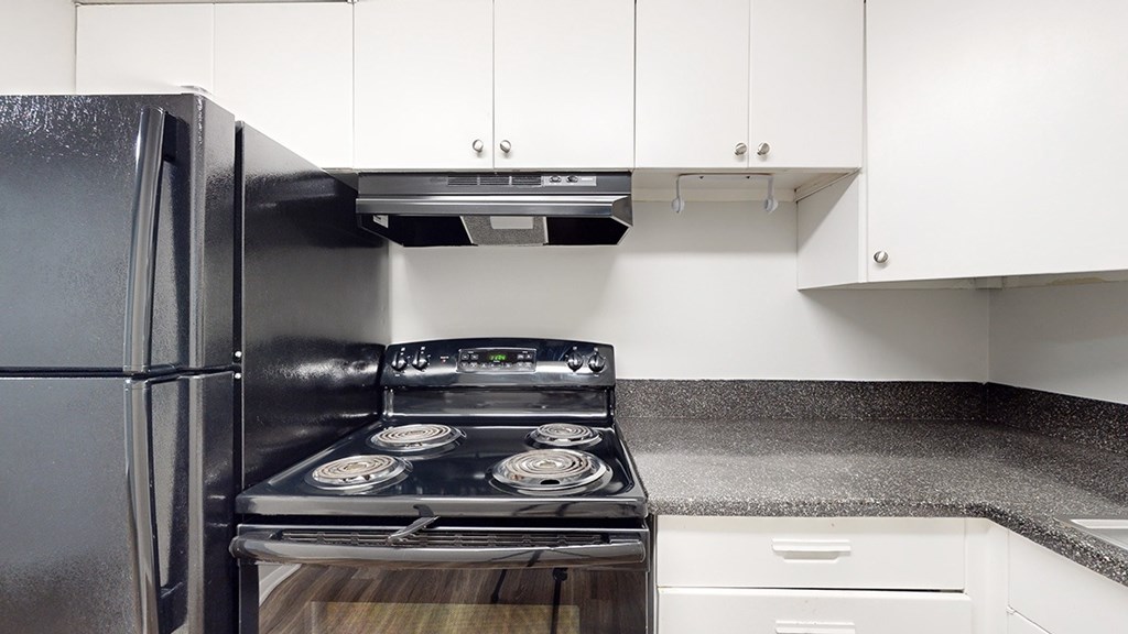 A black refrigerator is in a kitchen with a stove top oven.