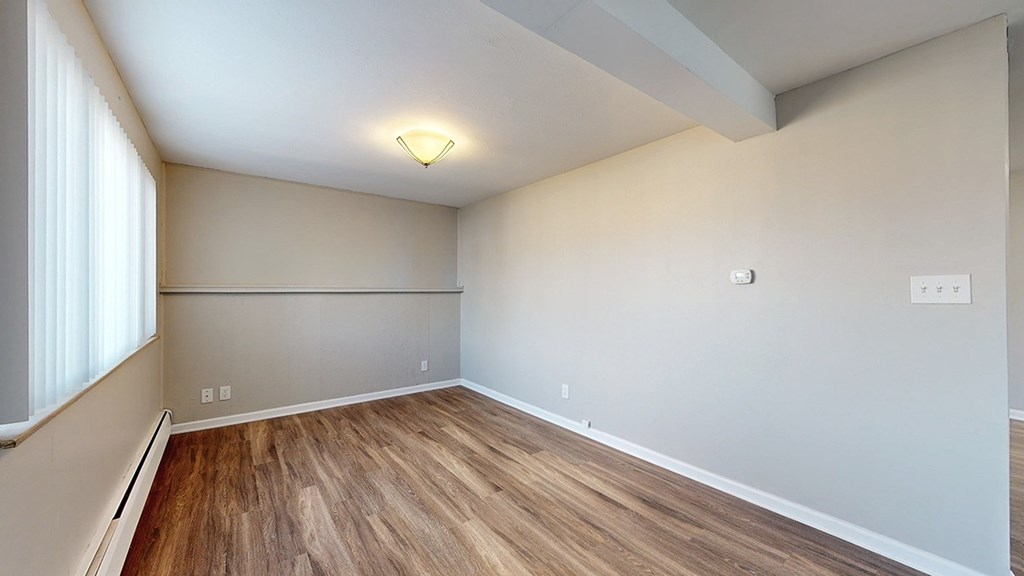 A room with wooden flooring and a window on the left side.