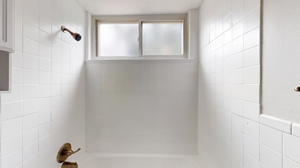 A white tiled bathroom with a window above the bathtub.