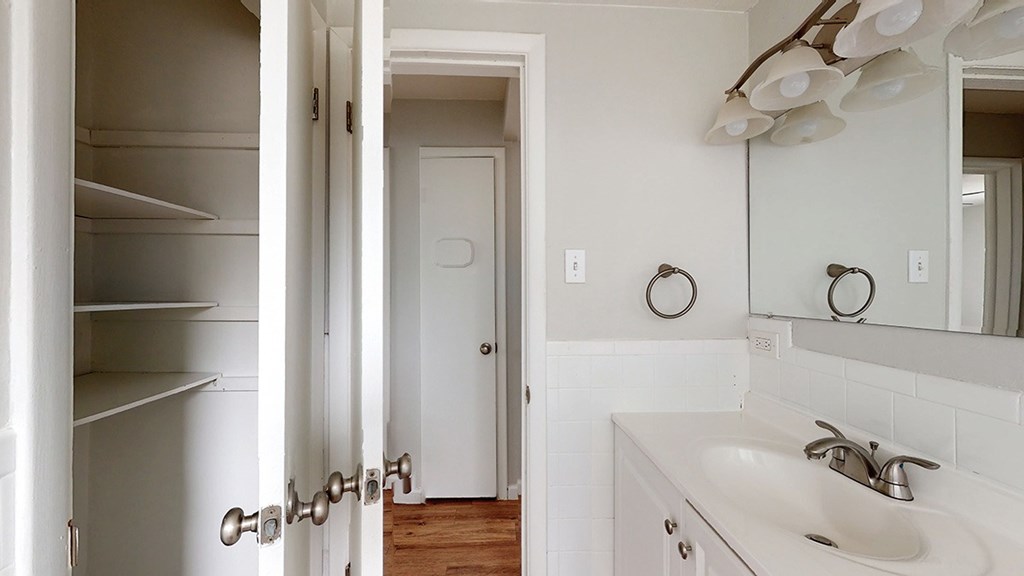 A white bathroom with a sink, mirror, and a door.
