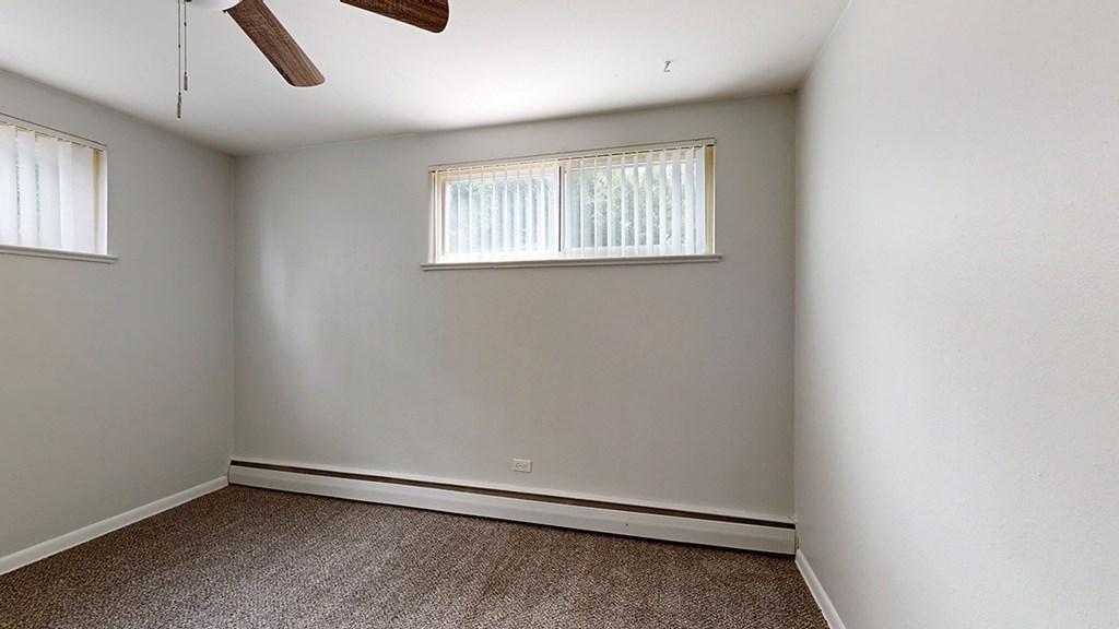 A room with a ceiling fan and two windows.