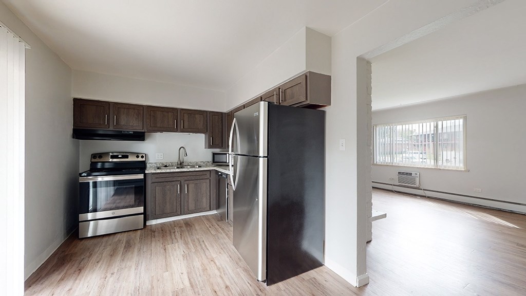 A kitchen with a black refrigerator, stainless steel oven, and wooden cabinets.