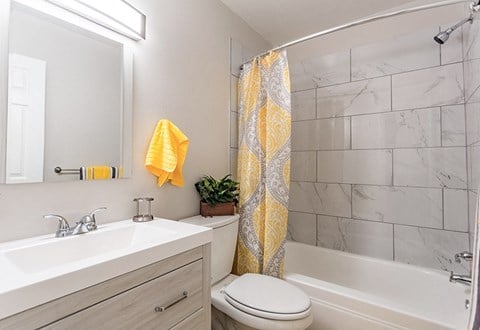 A bathroom with a white toilet, sink, and a yellow shower curtain.