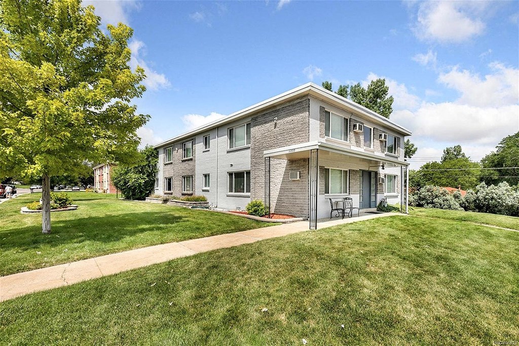 A modern house with a grey and white exterior is surrounded by a well-kept lawn and trees.