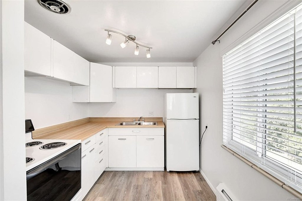 A white kitchen with a stove, refrigerator, and wooden floors.