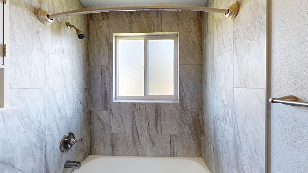 A bathroom with a tub, shower, and a window.