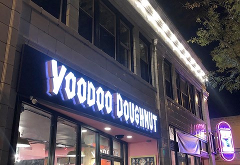 A Voodoo Doughnut storefront at night with neon lights.