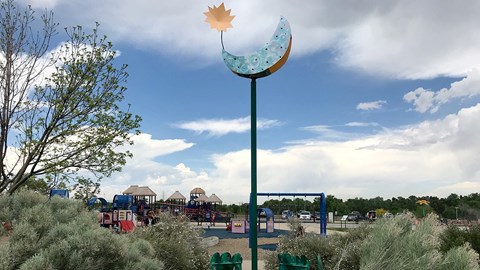 A playground with a blue swing set and a yellow leaf-shaped object on a pole.