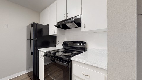 A black refrigerator and stove top oven in a kitchen with white cabinets.