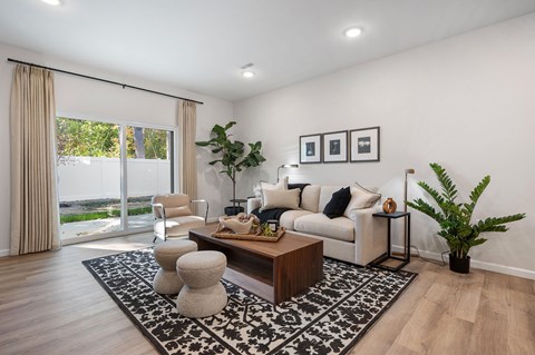 A living room with a white couch, a coffee table, and a large window with curtains.