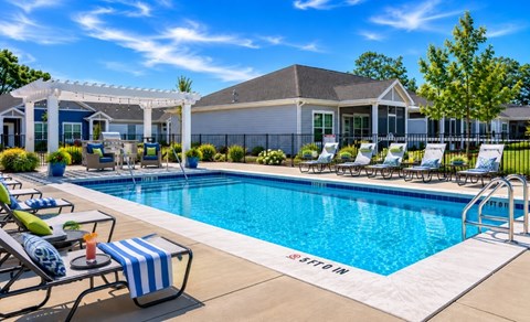 A pool with chairs and a house in the background.