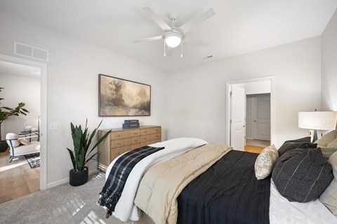 A bedroom with a bed, a ceiling fan, and a painting on the wall.