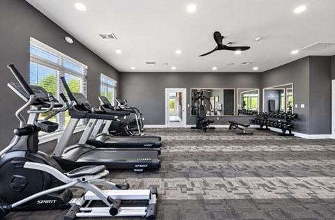 A spacious gym with treadmills, elliptical machines, and a fan.