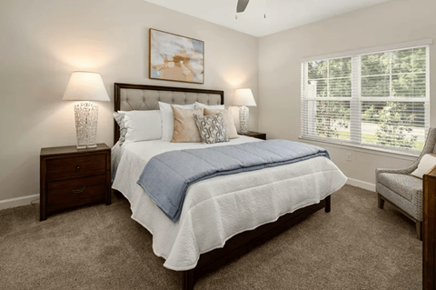 A bedroom with a bed, two lamps, a painting, and a window.