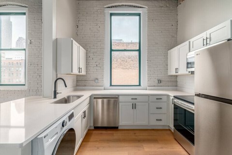 A kitchen with white cabinets and a window overlooking a dirt field.