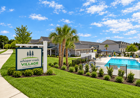 A sign for Whisper Creek Village is in the foreground of a well-manicured lawn.