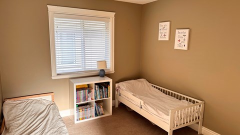 A small child's bedroom with a white bed and a bookshelf.