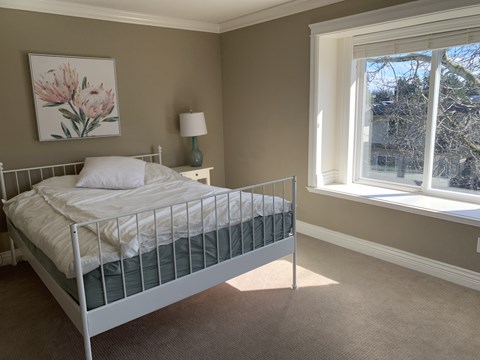 A bedroom with a white bed and a painting of pink flowers on the wall.