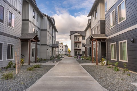 A long concrete walkway leads between two rows of modern townhouses at Woodburn Place Apartment Homes, Woodburn