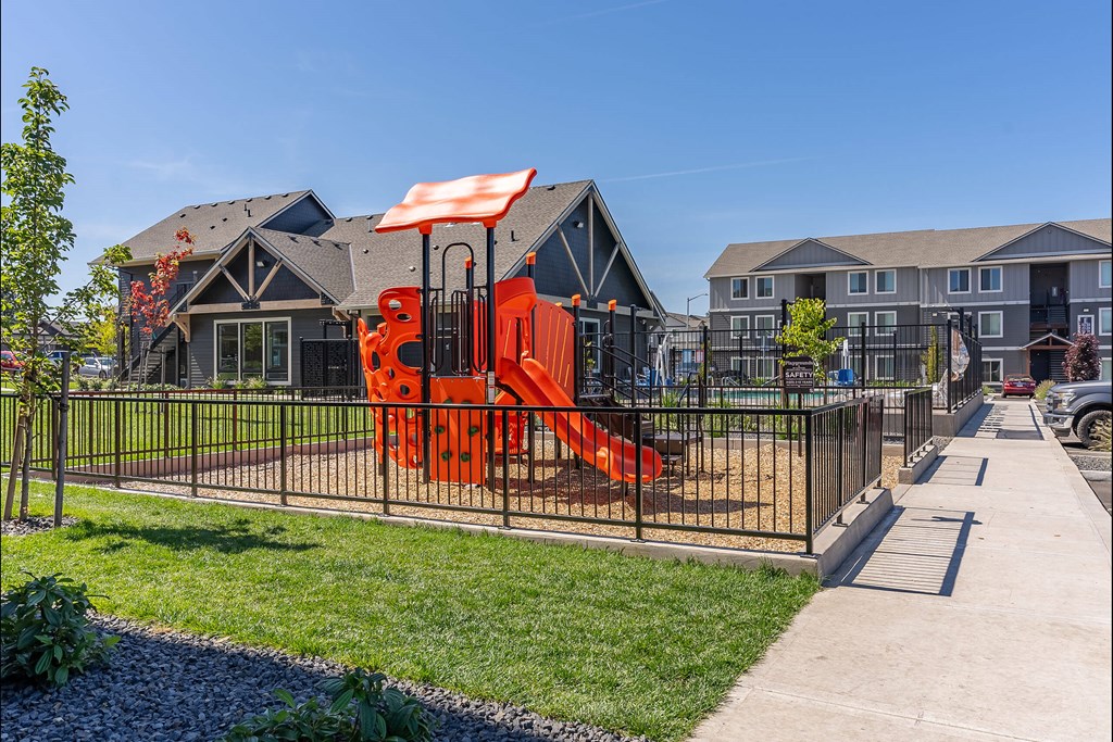 A playground with a red slide is in front of a building at Cascade Place Apartment Homes, Molalla, 97038
