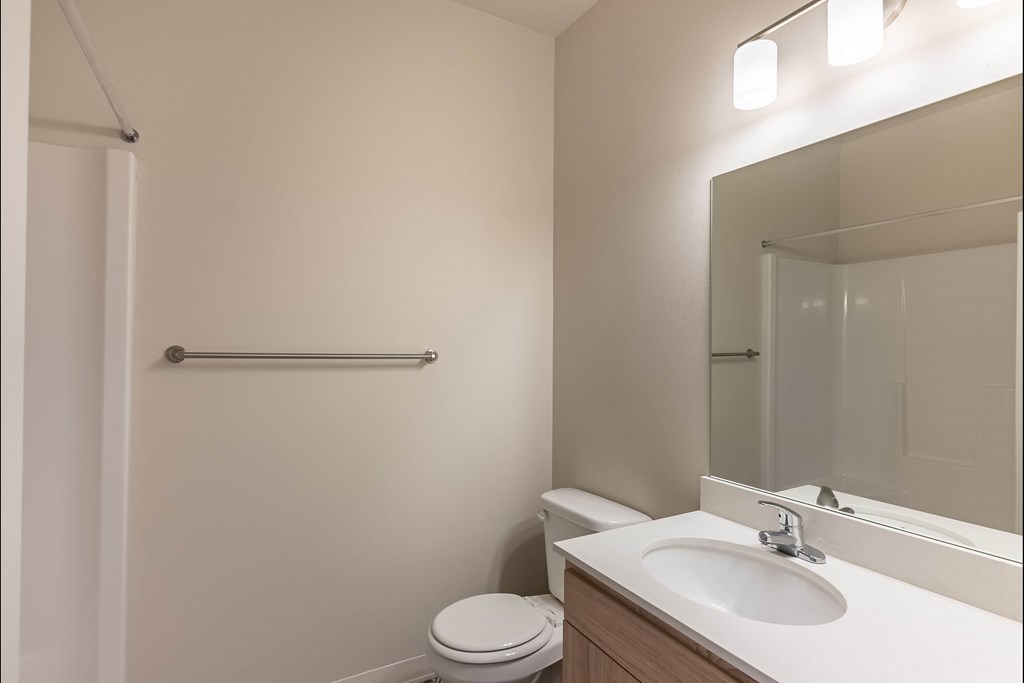 A white toilet sits next to a sink in a small bathroom at Cascade Place Apartment Homes, Molalla