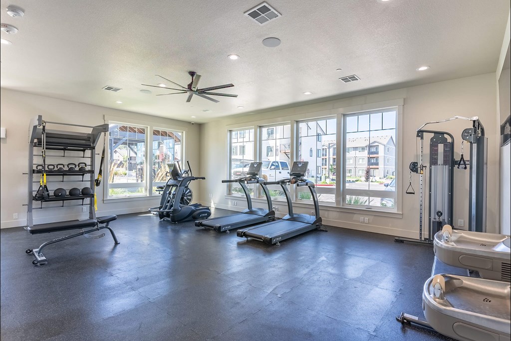 A spacious gym with treadmills, elliptical machines, and a weight rack at Cascade Place Apartment Homes, Oregon