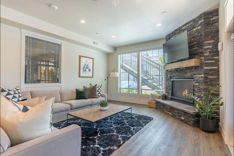 A modern living room with a grey couch, a fireplace, and a TV mounted on a stone wall at Forestplace Apartment Homes, Forest Grove