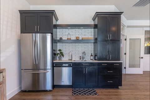A kitchen with a stainless steel refrigerator and black cabinets.
