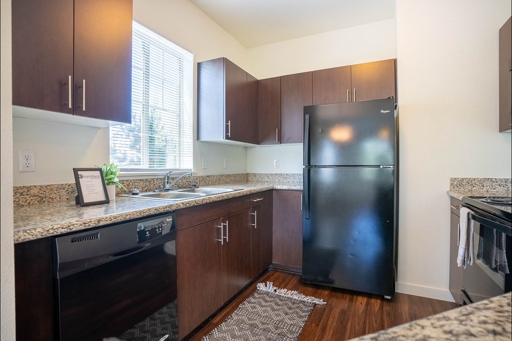 A kitchen with a black fridge and wooden cabinets at Riverplace Apartment Homes, Independence