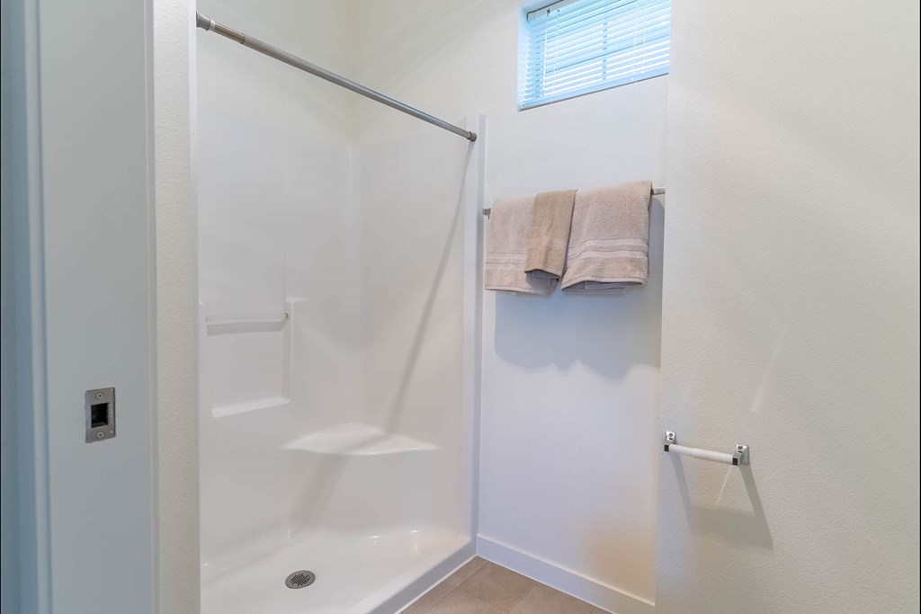 A white bathroom with a glass shower door and towels hanging on a rack at Riverplace Apartment Homes, Independence
