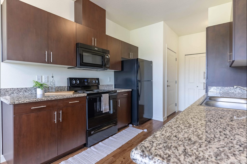 A kitchen with dark wood cabinets and black appliances at Riverplace Apartment Homes, Independence