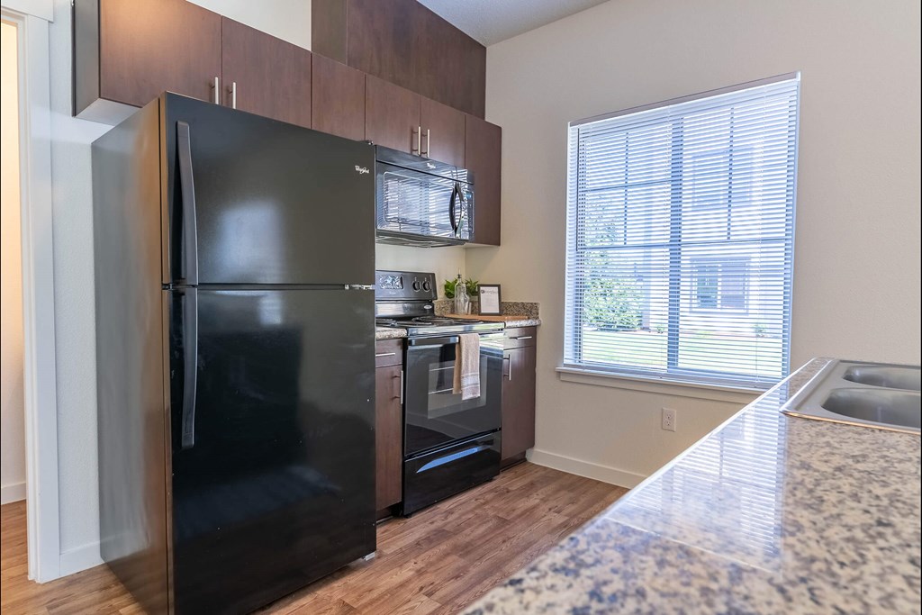 A black fridge in a kitchen with wooden cabinets and a window at Riverplace Apartment Homes, Oregon