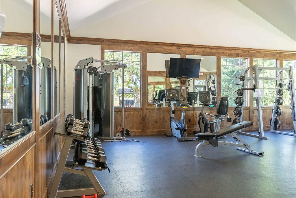 A spacious gym with a variety of equipment including treadmills, weights, and a television at Riverplace Apartment Homes, Oregon