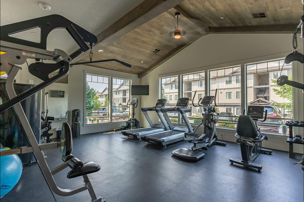 A gym with a variety of equipment including treadmills, weights, and a stationary bike at Sandyplace Apartment Homes, Sandy, OR, 97055