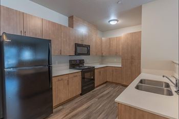 A kitchen with a black refrigerator, wooden cabinets, and a stainless steel sink.