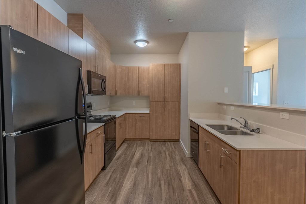 A kitchen with a black fridge and wooden cabinets at Sandyplace Apartment Homes, Sandy, OR