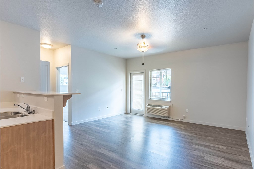 A spacious room with wooden floors and a window with blinds at Sandyplace Apartment Homes, Sandy, Oregon