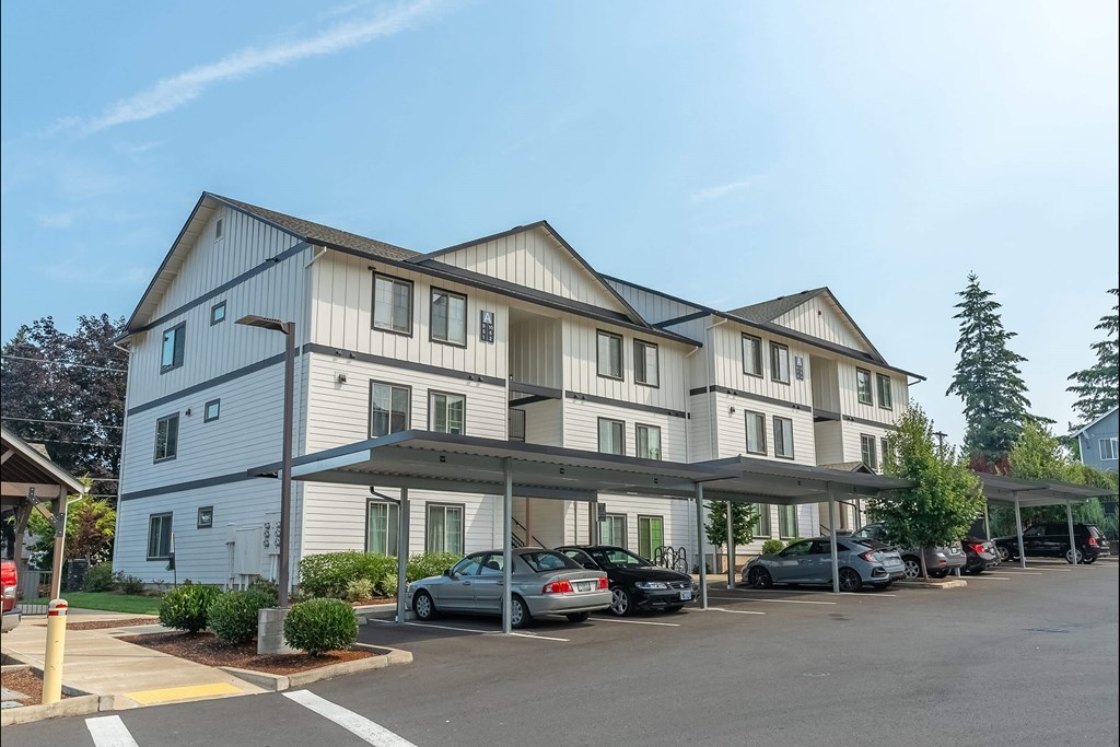 A large white building with a grey roof and a parking lot in front at Sandyplace Apartment Homes, Oregon, 97055