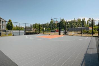 A basketball court is surrounded by a fence and has a red court.