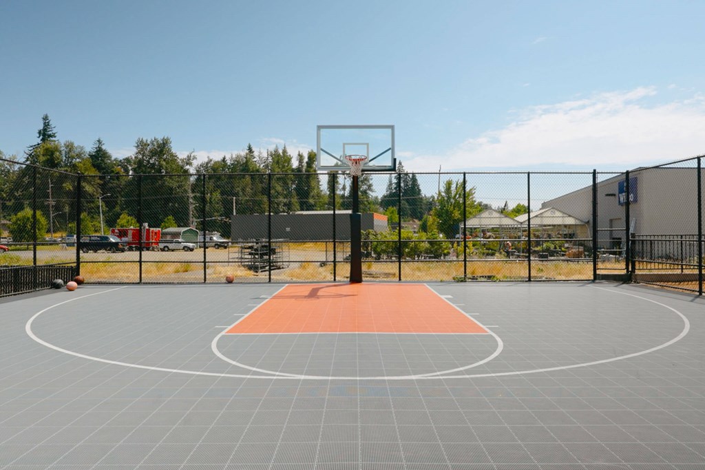 A basketball court with a hoop and a grey floor with orange area in the middle at Silverplace Apartment Homes, Silverton, 97381
