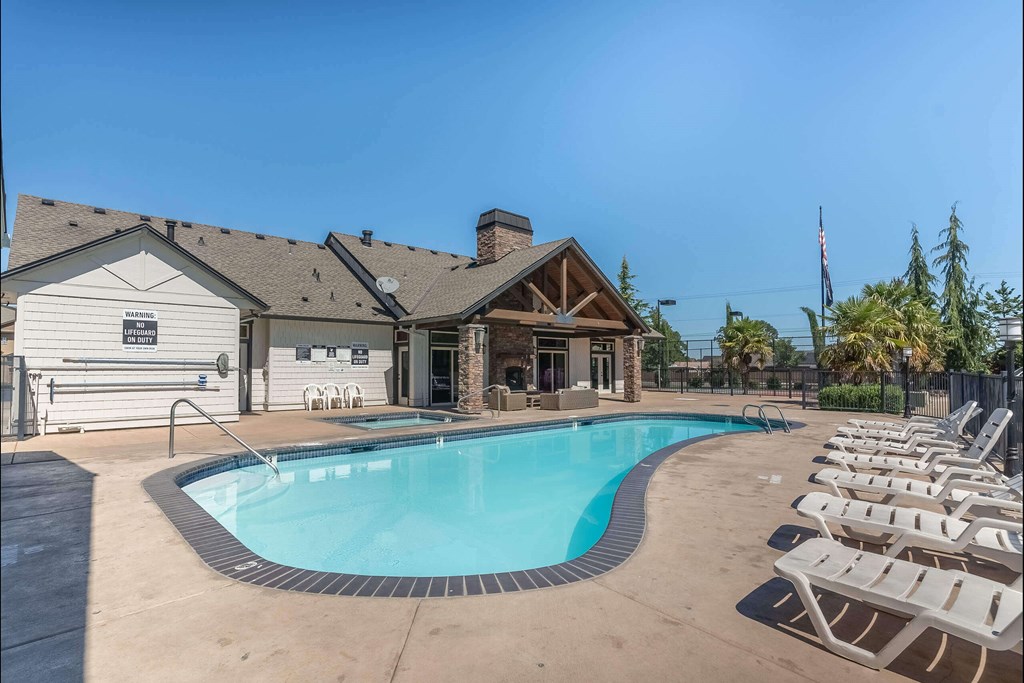 A pool with chairs around it and a building in the background. A pool with chairs around it and a building in the background at Stoneplace Apartment Homes, Molalla, OR, 97038