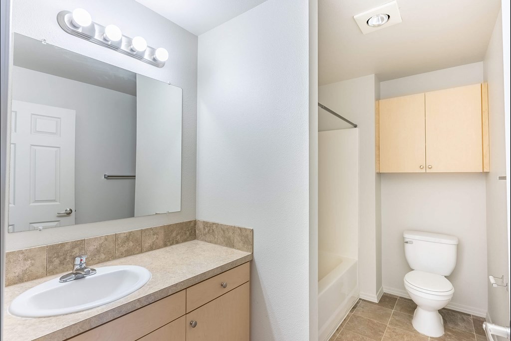 A bathroom with a sink, mirror, toilet and cabinetry at Stoneplace Apartment Homes, Oregon