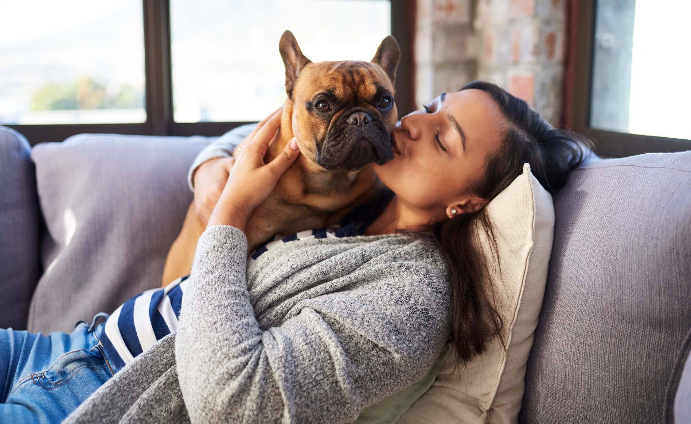 A woman is cuddling with a dog on a grey couch at The Hub Hermiston Apartments, Hermiston, Oregon