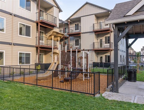 A playground area with a slide and a fence in front of apartment buildings.