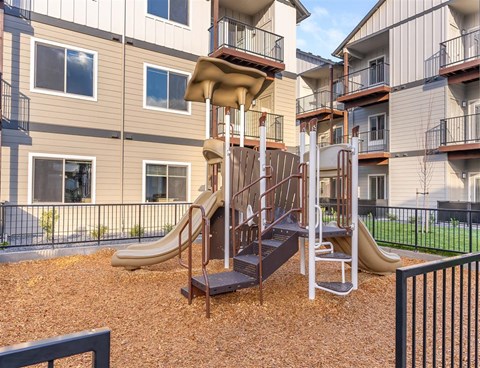 A playground with a slide and a climbing frame in front of apartment buildings.