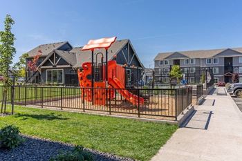 A playground with a red slide is in front of a building.
