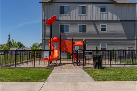 A playground with a slide and a building in the background.