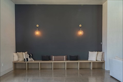 A long bench with cushions and a lamp on the wall.