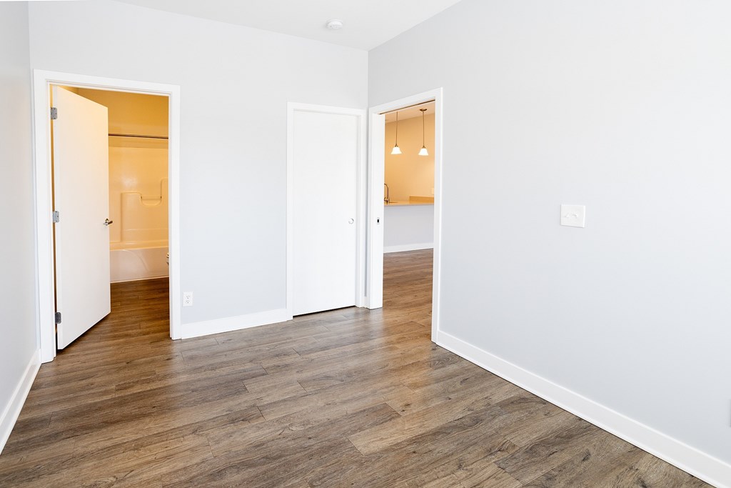 A room with white walls and wooden flooring with two open doors.