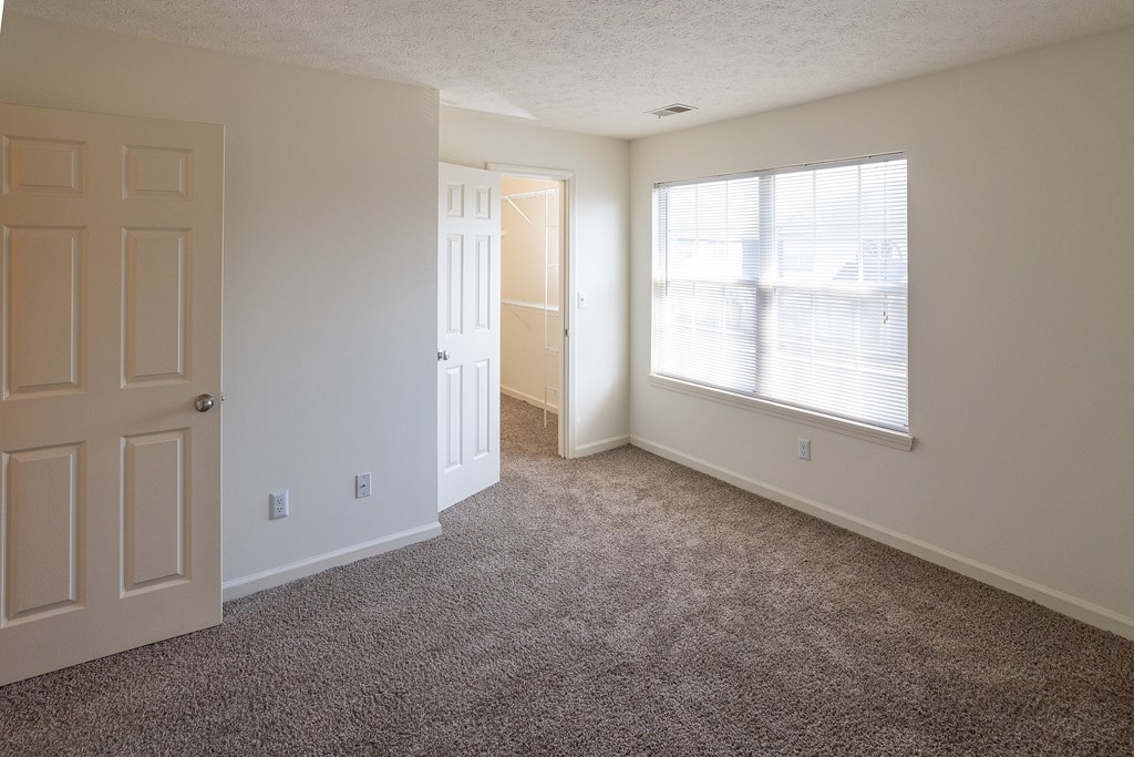 A room with a carpeted floor, a door, and a window.